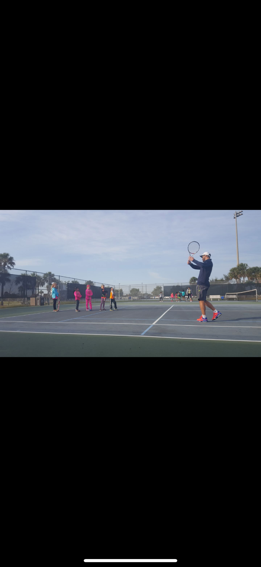 Professional tennis coach demonstrating forehand technique to junior tennis players on outdoor court